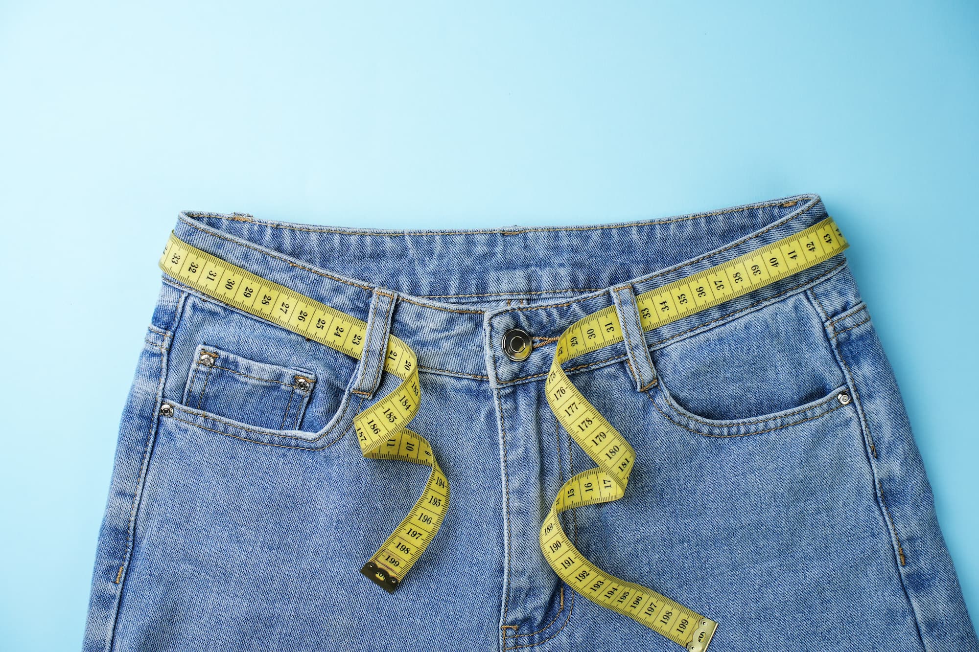 a pair of blue jeans with a yellow measuring tape being used as a belt a pair of blue jeans with a yellow measuring tape being used as a belt