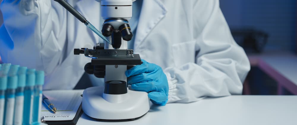 how long after unprotected sex to get tested A lab technician in a white coat using a pipette and microscope, illustrating clinical research on how long after unprotected sex to get tested for STIs.